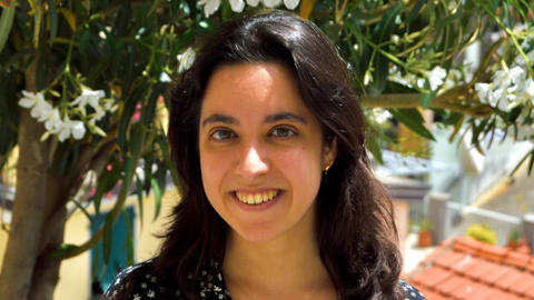 Silvia is a young woman with long dark hair and medium-toned white skin. In the photo, she is standing in front of a tree and smiling, wearing a black dress with white polka dots.