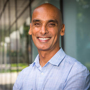 Salil Vadhan. Headshot. Salil is in a sunny indoor location. He is bald, with medium-brown skin. He is facing the viewer and smiling broadly.