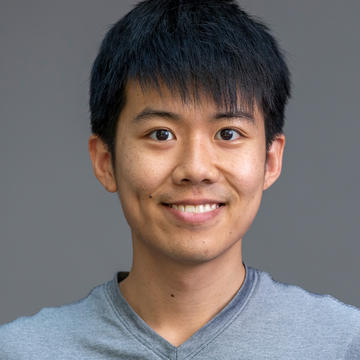 Sitan Chen. Headshot. Sitan is in front of a dark gray background. He has short black hair, coppery skin and dark almond-shaped eyes. He is wearing a light gray T-shirt and smiling broadly.
