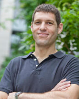 Yaron Singer. Headshot. Yaron is standing outside in front of a green landscape. His arms are folded across his chest. He has short dark hair and is smiling.