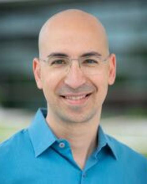 A front-facing headshot of Ariel. He has light skin, is bald, and is wearing glasses.