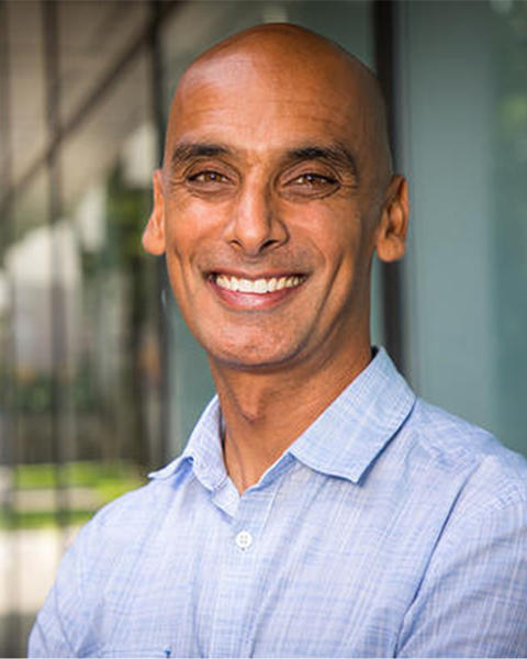 Salil Vadhan. Headshot. Salil is in a sunny indoor location. He is bald, with medium-brown skin. He is facing the viewer and smiling broadly.